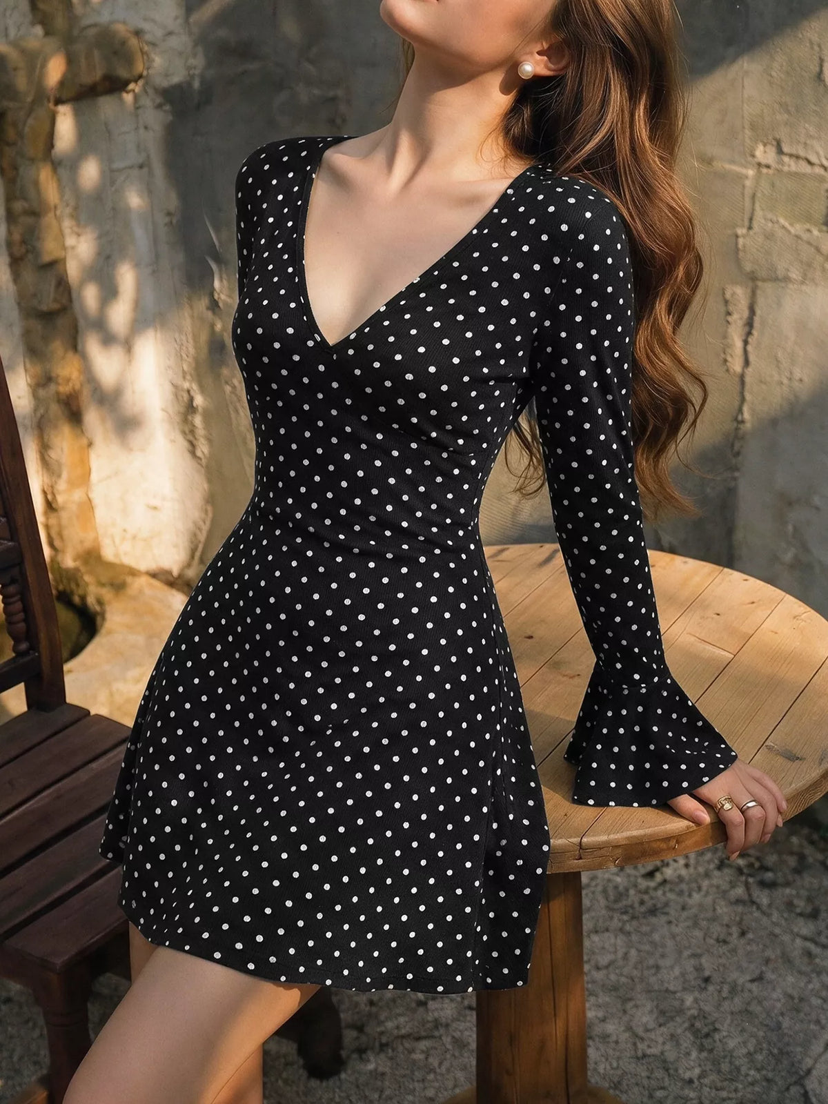 View 3 of the black long-sleeve polka-dot mini dress with a deep V and ruffled cuffs.