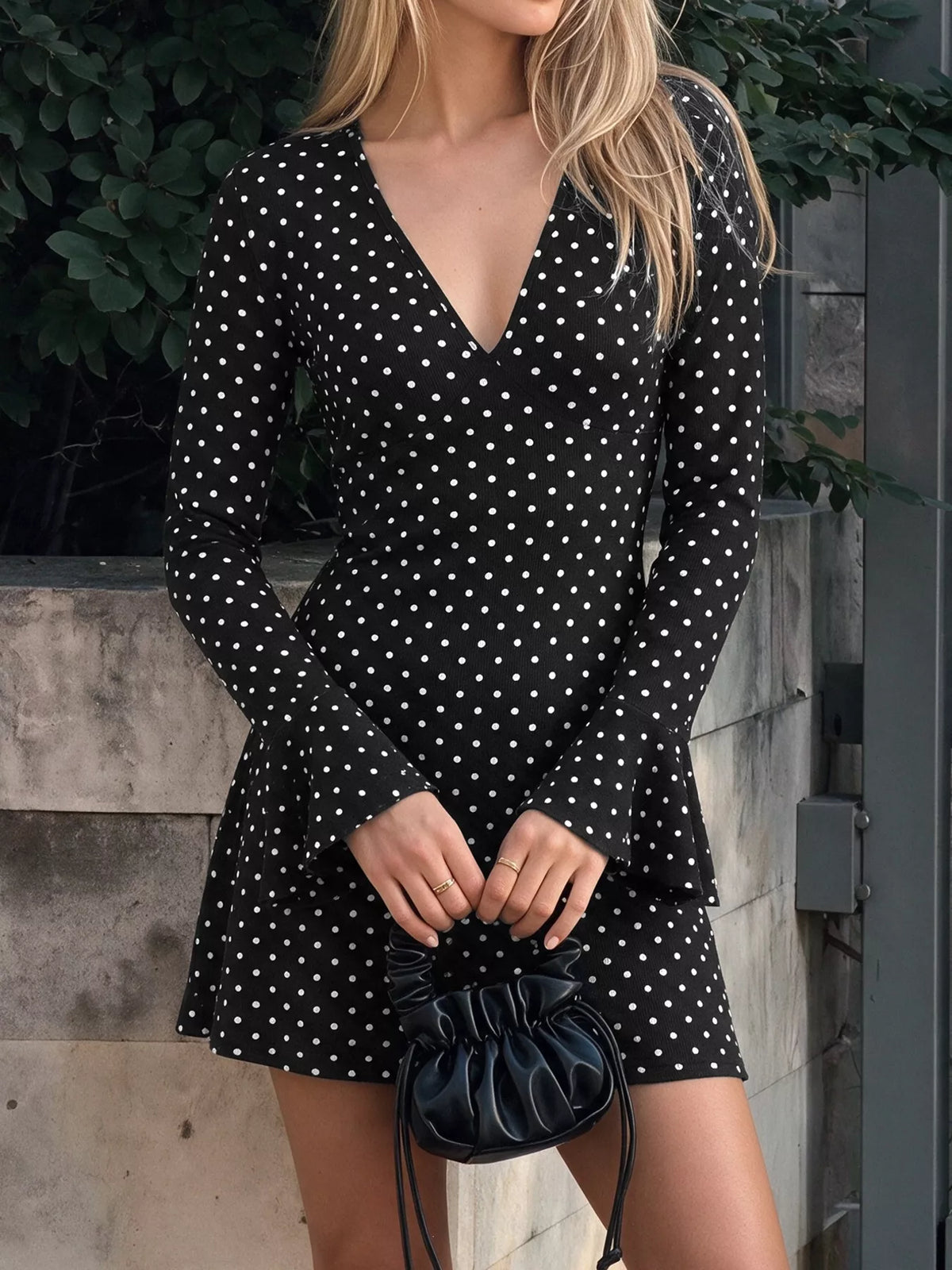 View 2 of the black long-sleeve polka-dot mini dress with a deep V and ruffled cuffs.