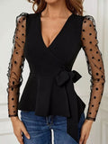 Black wrap top with a peplum, a waist tie, and sheer polka-dot mesh sleeves.