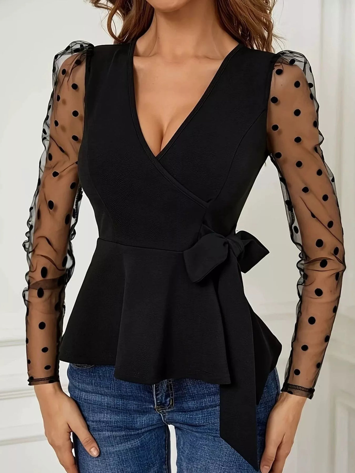 Black wrap top with a peplum, a waist tie, and sheer polka-dot mesh sleeves.