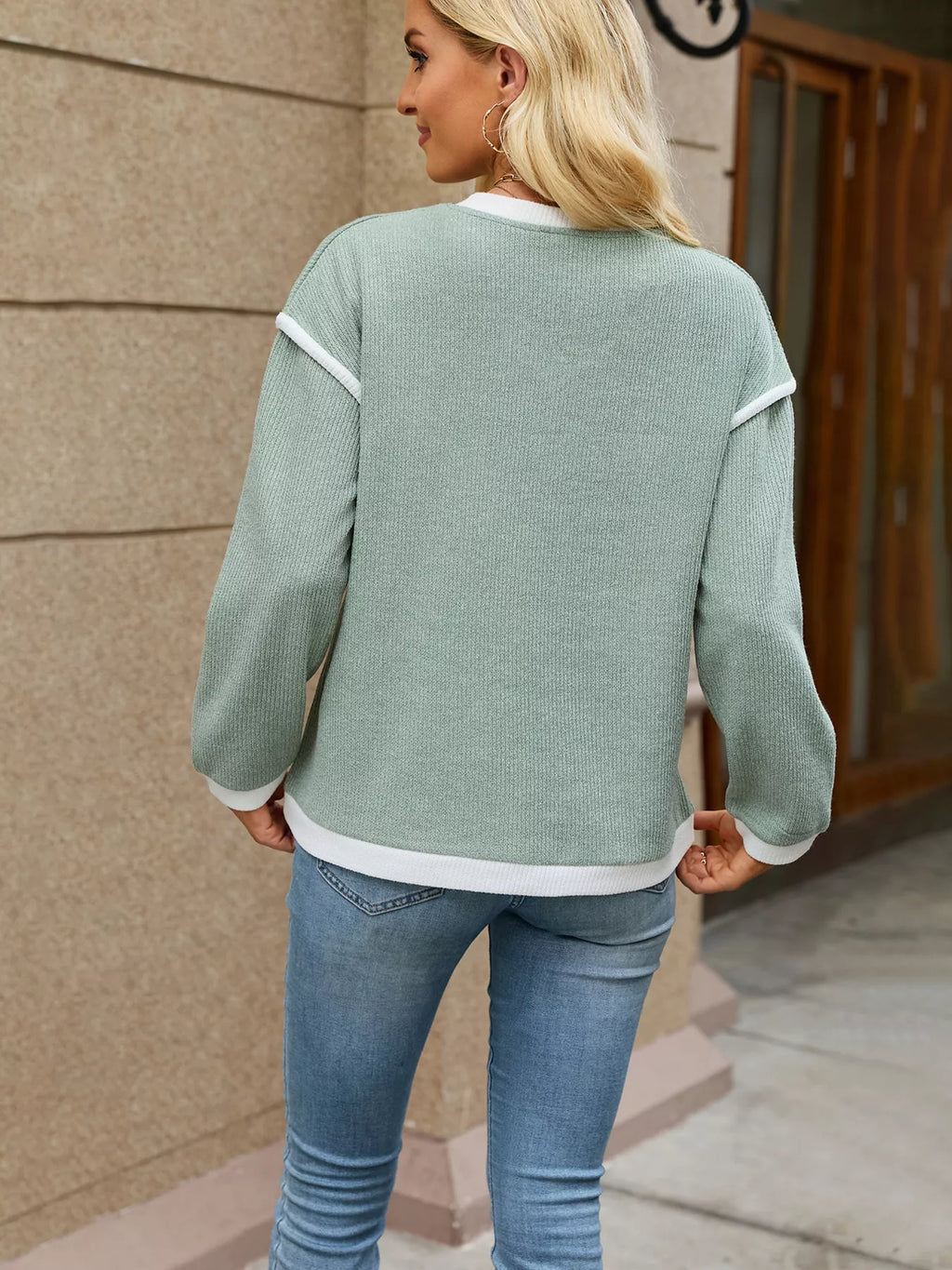 View 18 of the beige dropped-shoulder V-neck knit sweater with white binding at the neck, cuffs, and hem.
