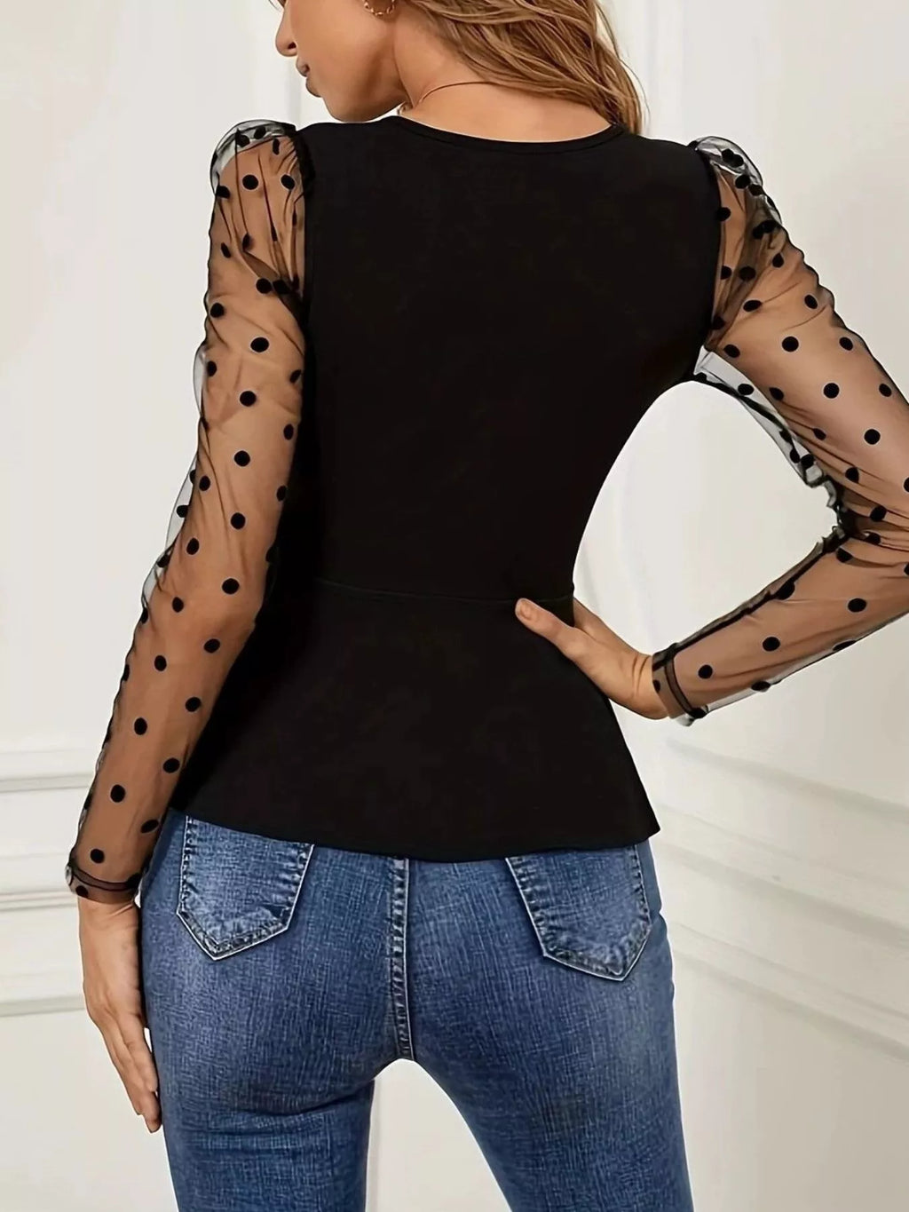 View 4 of the black wrap top with a peplum, a waist tie, and sheer polka-dot mesh sleeves.