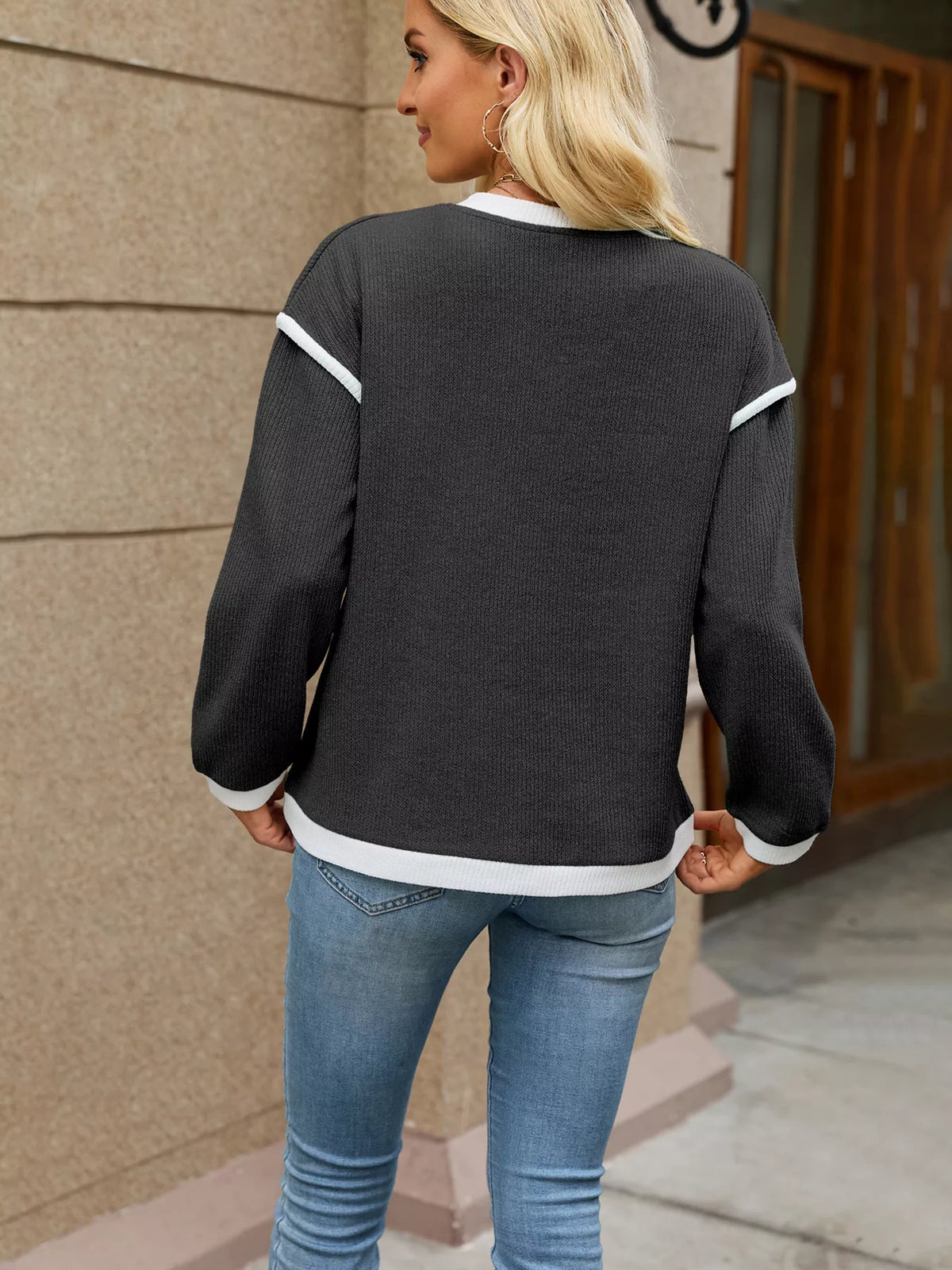 View 12 of the beige dropped-shoulder V-neck knit sweater with white binding at the neck, cuffs, and hem.